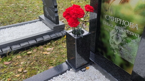 Гранитная прямоугольная ваза с цветами на фоне стеклянного памятника